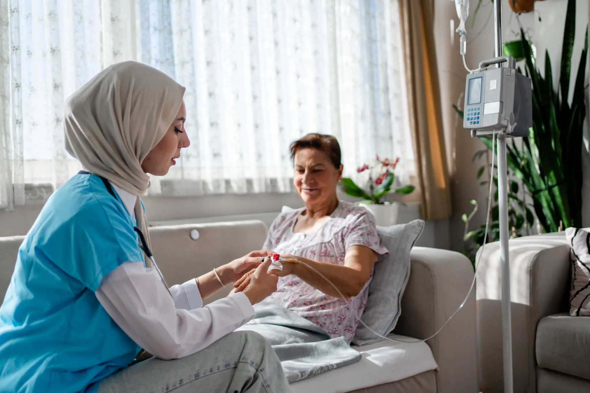 A nurse in a hijab caring for a patient in a hospital room.